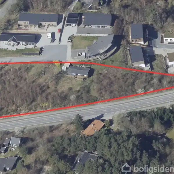 En trekantet grund markeret med en rød linje. Grunden er omgivet af huse og veje, og der er en skovklædt område mod bunden.