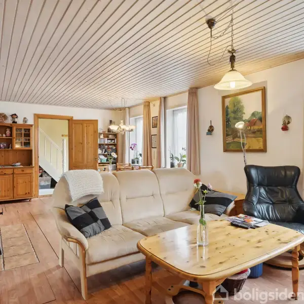 Stue med beige sofa og sort lænestol ved et træbord, omgivet af lyse vægge og træmøbler. Lamper hænger fra loftet, og vinduer giver naturligt lys.