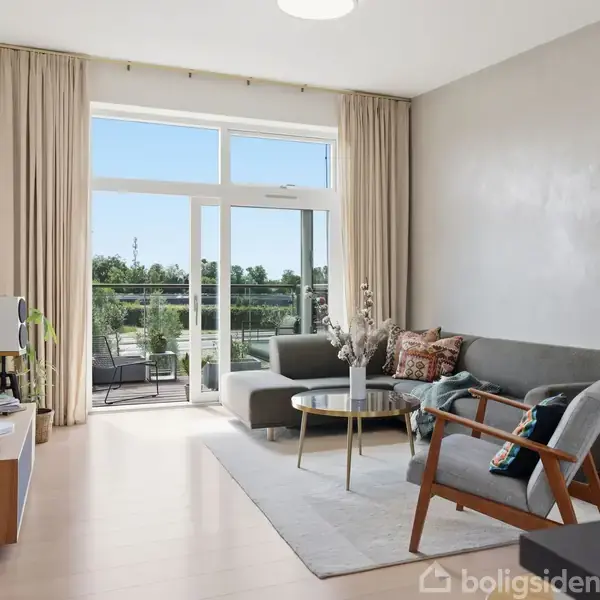 Stue med grå sofa og sofabord, der vender mod en fladskærms-TV. Stor glasdør fører ud til terrasse med udsigt til grønne områder. Lyst trægulv og lyse gardiner.