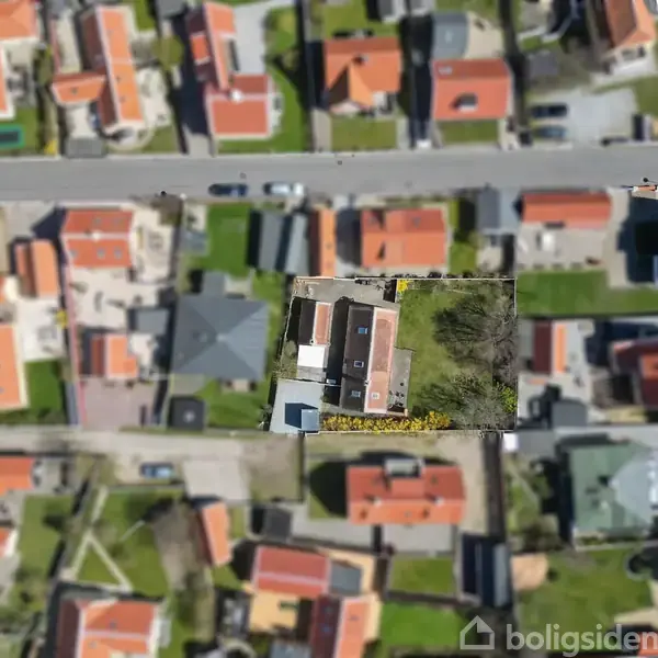 Et kvarter ses fra oven med huse med røde tage og grønne haver. Området er beboet med flere parallelle gader. En vej krydser, hvor biler ses kørende.
