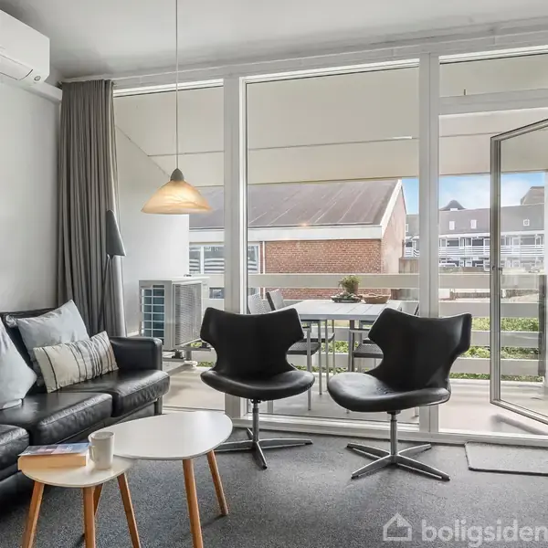 Et moderne stueområde med sort lædersofa og sofabord. To sorte stole vender mod en stor glasdør, der åbner ud til en altan. Lyst og minimalistisk interiør.