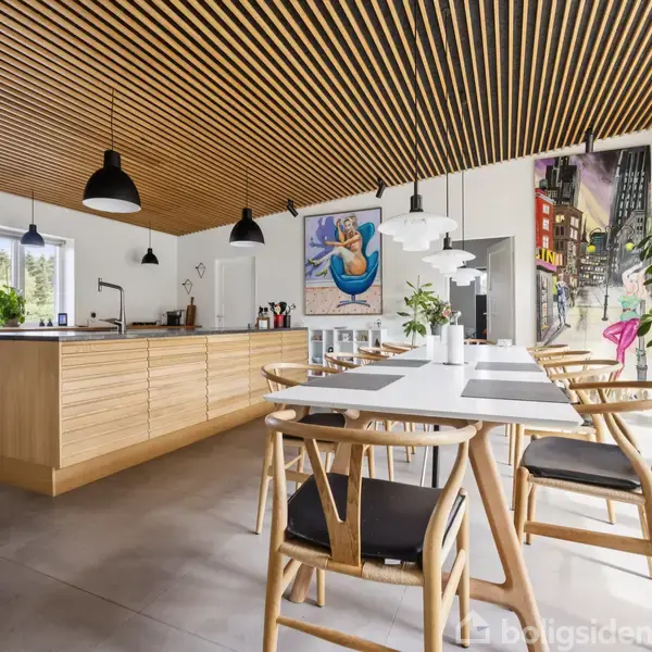 Et moderne køkken med et stort træbeklædt loft, hvor der hænger sorte lamper. Køkkenøen har lyse trælåger. Der er spisestuemøbler i træ og mange grønne planter omkring.