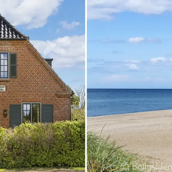 Murstenshus med grønne skodder, tekst "Dyreborg Huse" på facaden, står ved siden af en strand med udsigt over havet under en blå himmel med lette skyer.