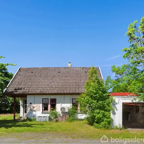 Hus med skråt tegltag står blandt grønne træer. En garage ses til højre. Blå himmel og græsplæne omgiver huset, som har en enkel facade med vinduer.