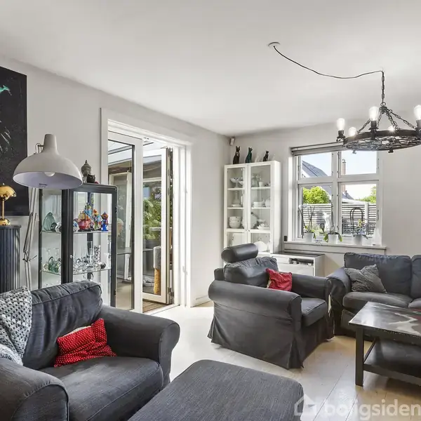 En stue med to sofaer og et sofabord, dekoreret med farverige malerier af løver. Der er vinduer og en glasdør mod en terrasse, lamper og en skabsvitrine.