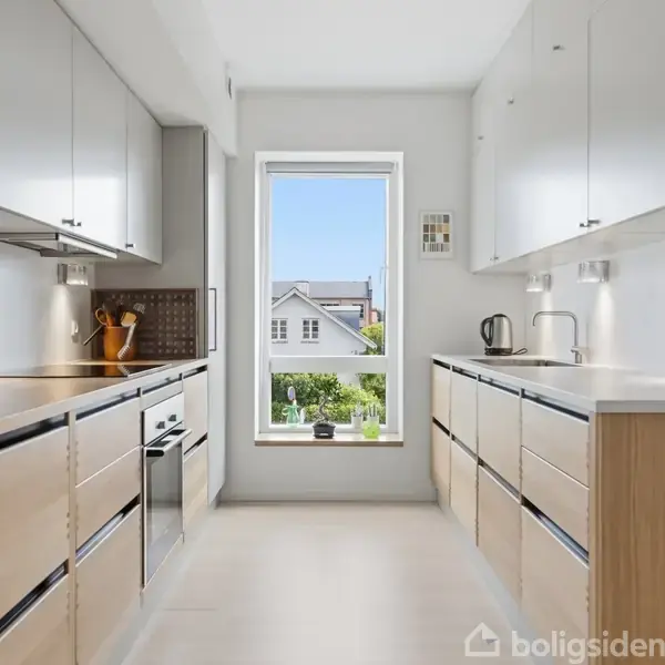 Moderne køkken med lyse trælåger og hvid bordplade. Enkelt placeret vindue viser udsigt til have og nabohus. Elegant indretning med køkkenudstyr og urtepotter. Enkel og lys atmosfære.