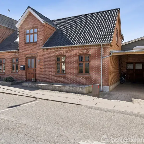 Rødt murstenshus med sort sadeltag og flere buede vinduer, står ud til gaden. Ved siden er en overdækket indkørsel. Husene står tæt på hinanden i en bymæssig omgivelser.