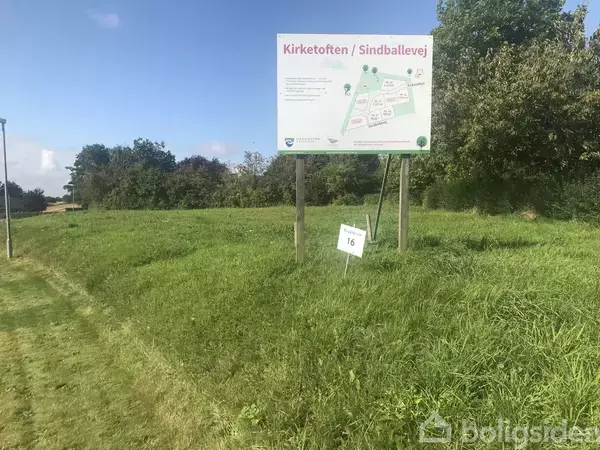 Græsmark med et stort skilt viser et kort over Kirketoften/Sindballevej. Tekst på skiltet: "Kirketoften / Sindballevej." Skiltet står i en landlig, grøn kontekst med træer i baggrunden.