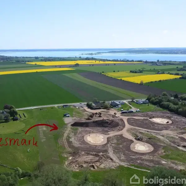Markeret område med teksten "Fællesmark" ved en stor mark med cirkulære byggepladser. Åbent landskab med marker i gule og grønne nuancer og en sø i baggrunden.
