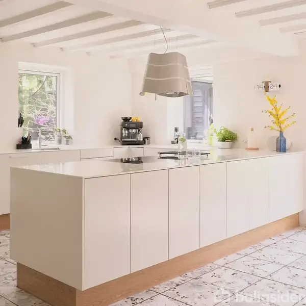 En lys stue med en grå sofa og planter ved et vindue. Til højre et spisebord med træstole, hængende lampe, og reoler. Fliser på gulvet og lyse vægge.