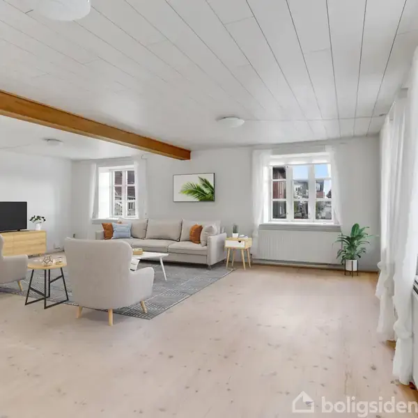 Stue med lyse møbler og træmøbler. To lænestole vender mod en sofa og et TV. Store vinduer giver lyst naturligt lys. Ruminddelingen er åben med hvide vægge og lofter.