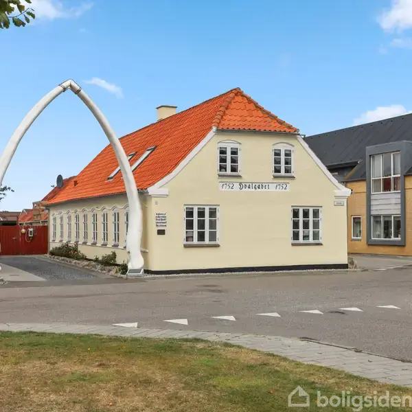 Et gult hus med rødt tag står ved en vej. Huset har en port lavet af store knogler. Tekst på huset: "1752 Dragsted 1752".