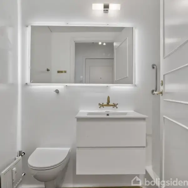 Hvidt badeværelse med toilet, vask og spejlskab. Vasken har en guldhane, og spejlet har lysramme. Dør til højre, toiletpapirholder til venstre. Ingen tekst fundet.