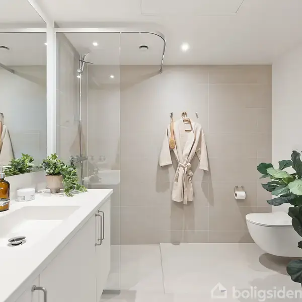 Et moderne badeværelse med hvid vask og spejl på venstre side, bruser i midten, og vægmonteret toilet til højre. To badekåber hænger på en knage. Grønne planter pynter rummet.