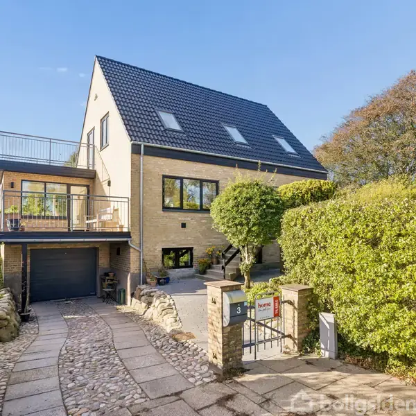 Hus med sort tag og gule mursten har en garage i nederste etage. Det er omgivet af grønne buske og et hegn ved indkørslen. Nummer 31 vises ved indgangen.