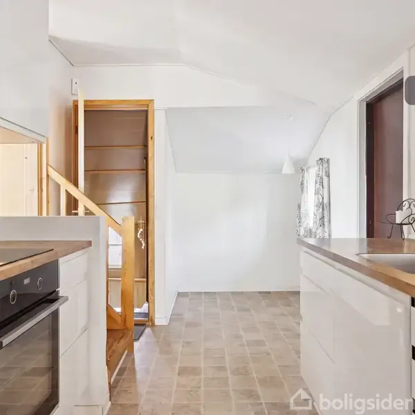 Et moderne køkken med hvide skabe og træbordplader. Der er en indbygget ovn, kogeplader og en vask. Trappen fører opad, og der er en spiseplads bagved. Tekst: "Visualisering".