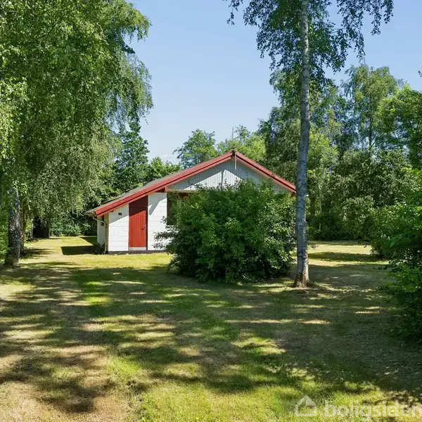 Hus med rødt tag og hvid facade står blandt grønt, omgivet af græs og træer i en have.