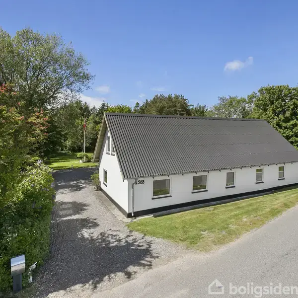 En hvidmalet, ét-plans hus med sort tag (nummer 352) står stille ved en vej. Haven omkring huset er grøn og frodig med træer og buske, mens himlen er blå.