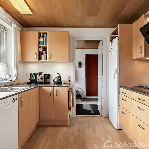 Køkkenet har lyse træskabe og -skuffer, indbygget opvaskemaskine, og komfur. Kaffemaskine og elkedel står på køkkenbordet. Et stort vindue giver udsigt til grønne planter udenfor. En dør fører til en gang med mørkt gulv.