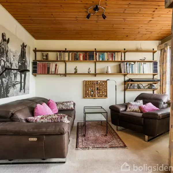 To lædersofaer med lyserøde puder står overfor hinanden. På en væg hænger en stor sort-hvid hesteplakat. En reol bagved er fyldt med bøger og dekorationer.
