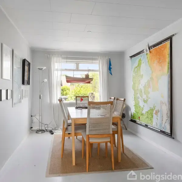 Et spisebord med seks stole er centreret i et lyst rum. En stor verdenskort-plakat hænger på væggen, og der er et vindue med udsigt til en grøn have.