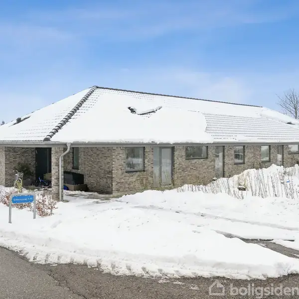 Et lille stenhus med snedækket tag står i et vinterlandskab. Huset ligger ved siden af en sneklædt vej. En gadelampe ses til højre, og et vejskilt viser "Bladhøjvej 22".