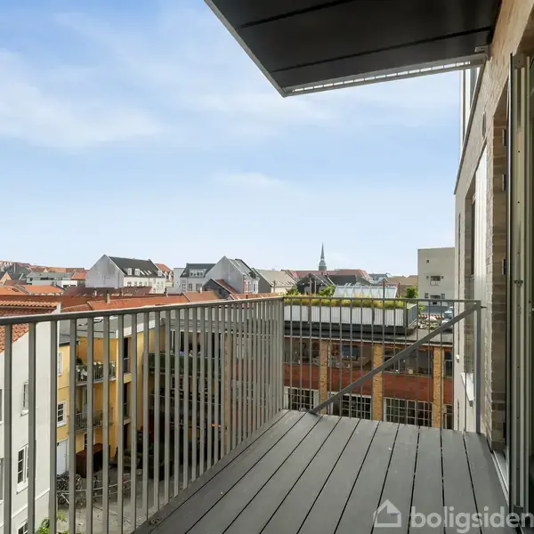 Balkonen er stille og giver udsigt over hustage i en by med blå himmel. En glasdør fører ud til balkonen, hvor man kan nyde de omkringliggende bygninger.