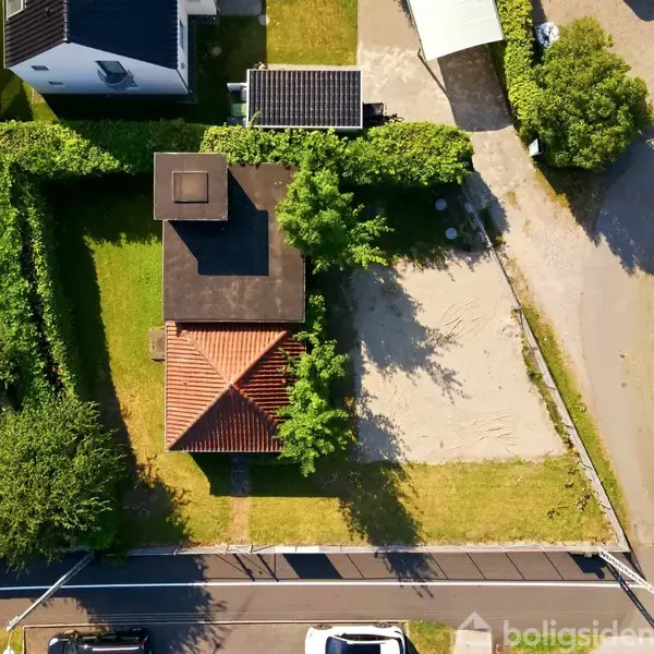 Hus med rødt tag placeret i en velplejet have omgivet af hække. Ved siden af er en indkørsel og en garage. Omkringliggende område har flere veje og grønne områder.
