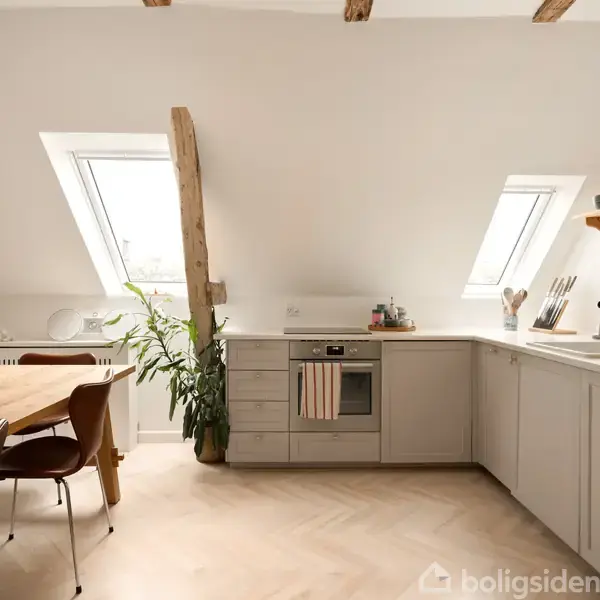 Moderne køkken i lyse farver med et spisebord til venstre. Vinduet skråner i taget, planter ved siden af bordet, og indbygningsovn i midten.