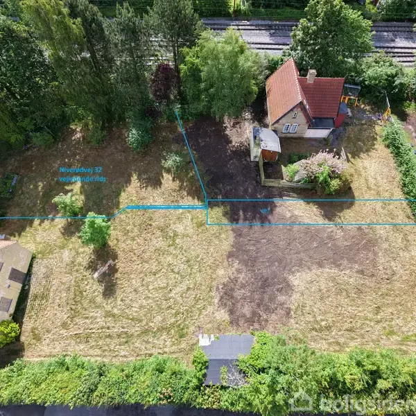 Hus omgivet af have, skov og marker. Blåt linjeskema angiver grænser. To huse med røde tage, skov mod toppen og græsset areal i midten. Tekst: “Nyelandsvej 32 www.Boligkilder.dk".