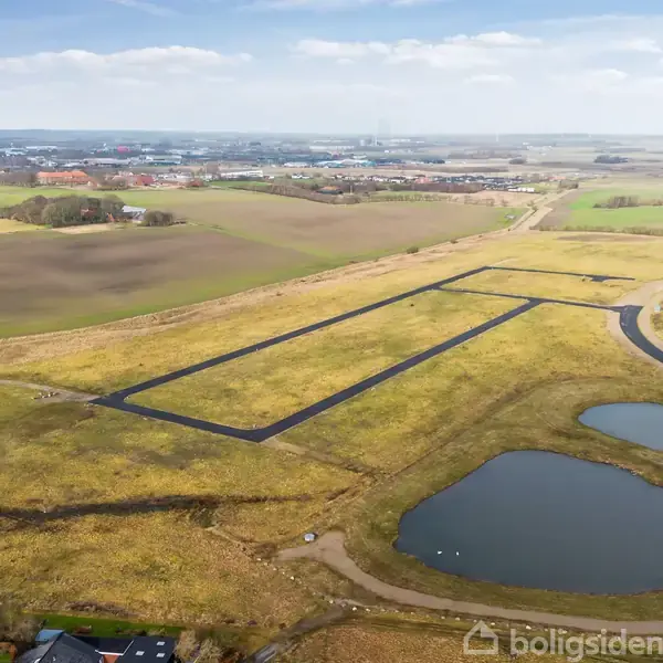 Et stort markområde med to rektangulære markerede felter omgivet af gulgræsset landskab, flere små søer og en vej. I baggrunden ses en by og horisonten.