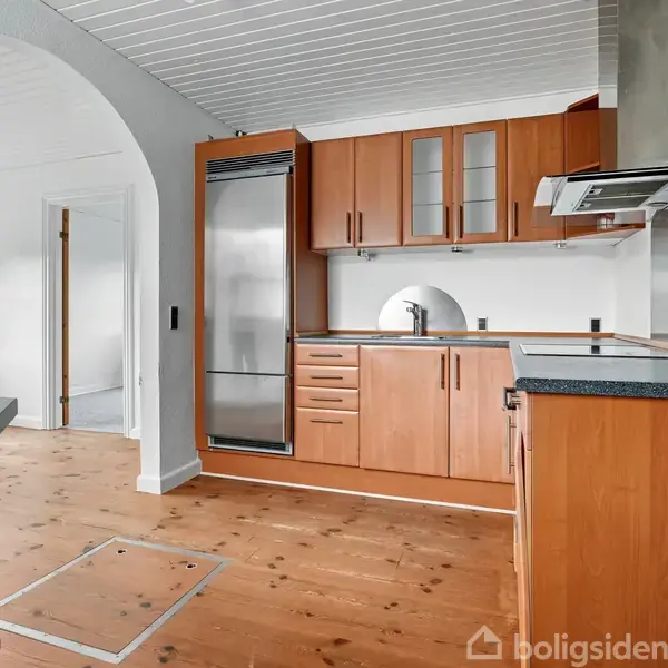 Køkken med træskabe og sort bordplade, handling: står tomt og rent, kontekst: lyst rum med trægulv og hvide vægge i et boliginteriør.