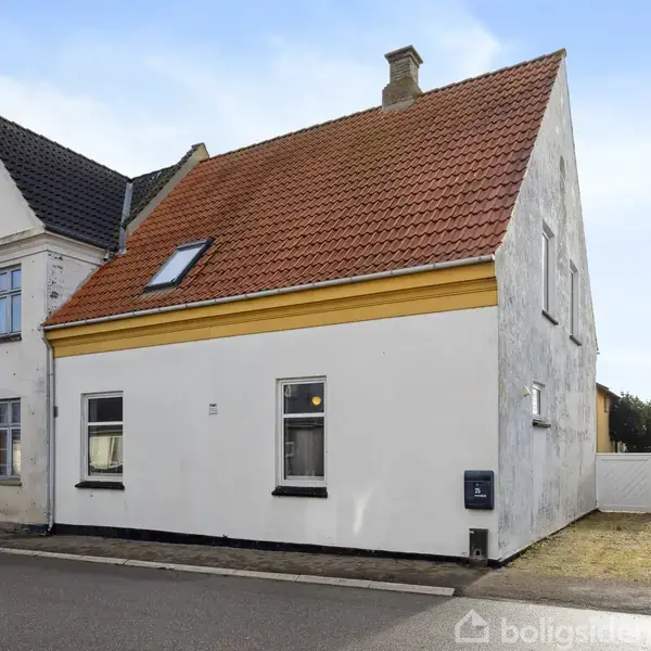 Et hvidt hus med rødt tag og en enkelt kvist står ved en asfalteret vej. Nabohuset har et sort tag. Der er en havelåge i baggrunden.