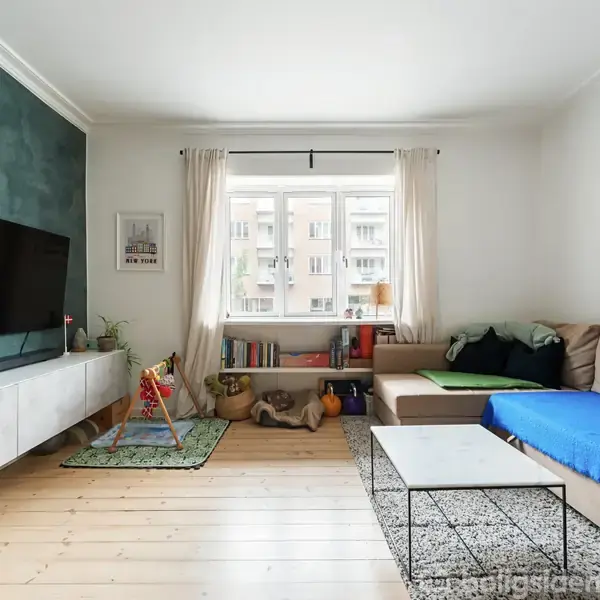 Et moderne stueområde med en stor beige sofa dækket af et blåt tæppe. Et sofabord står foran sofaen. Til venstre hænger et fladskærms-tv på væggen. Under vinduet er der en børnelegetøjshjørne og reol.