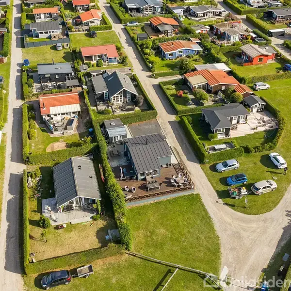 Boligområdet består af rækkehuse i varierende farver og designs, omkranset af velholdte græsarealer og adgangsveje. Nogle biler er parkeret nær husene, der danner et organiseret mønster.