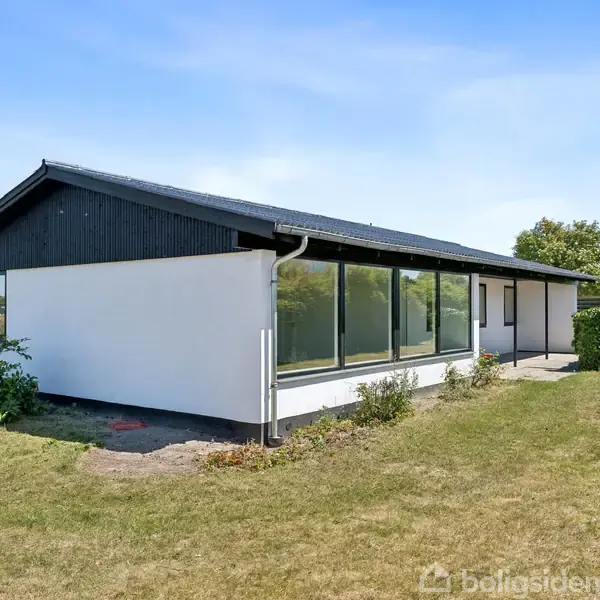 Et moderne, enkelt hvidt hus med store vinduespartier udenfor på en velplejet græsplæne under en klar blå himmel. Der er ingen tekst bortset fra "Boligsiden" vandmærket.