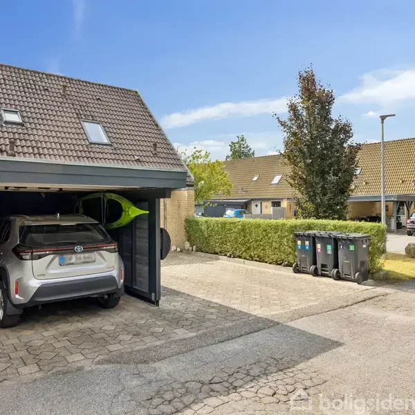 En moderne stue med en lysgrå sofa og et sort læderbord, omgivet af billeder på væggene og en stor fladskærm ved siden af et vindue med blomster.