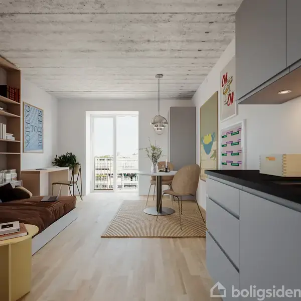 Værelse med sofa til venstre, skrivebord ved vindue og spisebord i midten. Køkken med grå skabe til højre. Lyse vægge og kunst på væggene. Naturligt lysindfald.