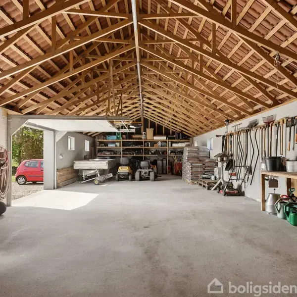 Garage med åbent tagkonstruktion lagrer værktøj hængende på væggen og køretøjer parkeret. En rød bil ses udenfor gennem den åbne port. Arbejdsbænk og hylder fylder baggrunden.