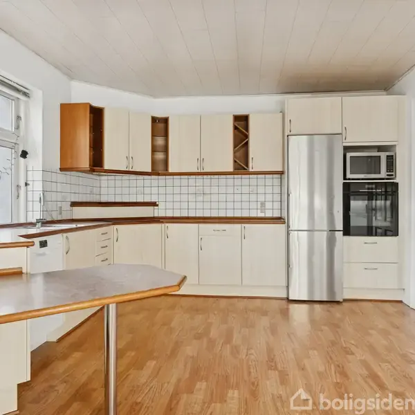 Køkkenet har lyse træskabe og en stålkøleskab. Det er udstyret med højt placeret ovn og mikroovn. Et stort vindue giver naturligt lys til det rummelige rum.