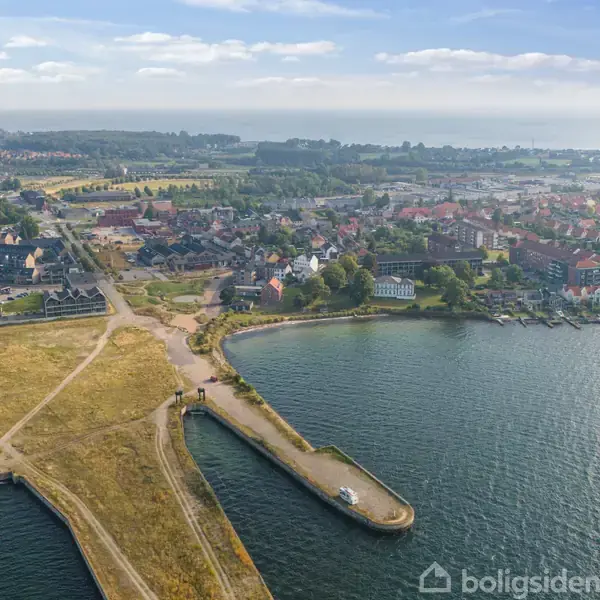 Kystby. Set fra luften. En by med huse ligger tæt ved vandet, med en mole, der strækker sig ud i en bugt. Grønt område adskiller bebyggelse fra kystlinjen.