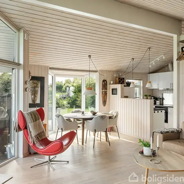 Rød lænestol står i en stue med lyse trægulve. En sofa og spisebord er placeret nær store vinduer, der giver udsigt til en have. Trofæer dekorerer væggen.