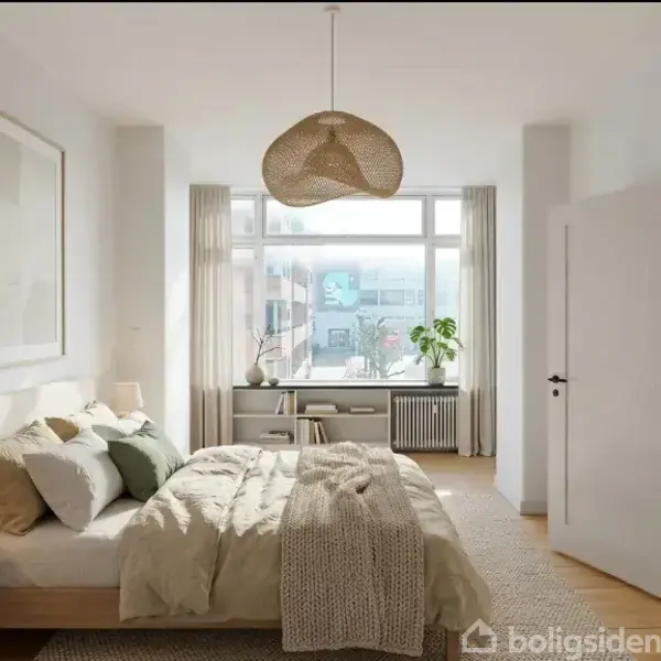 Soveværelse med dobbeltseng, sengeborde med lamper og tæppe. Vindue i baggrunden med skrivebord og plante. Hængende lampe i loftet og åben dør til sidst i rummet.