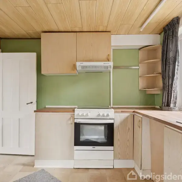 Køkken med træloft og grønne vægge, indeholdende en ovn med emhætte, træskabe og en vask. Stort vindue med gardiner på højre side, dør til stue i baggrunden.