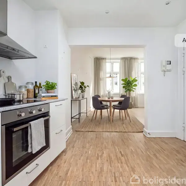 En moderne, hvidt køkken med komfur og emhætte; der er en tekande og krydderier på bordet. I baggrunden ses en spisestue med bord, stole og grønne planter. Tekst: "AI visualisering".