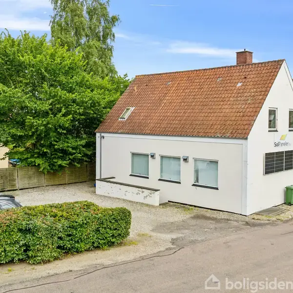 Et hvidt hus med rødt tegltag står ved en vej. Biler holder parkeret ved siden af, og grønne træer omkranser bygningen. Tekst på huset: "SelvVærdet".