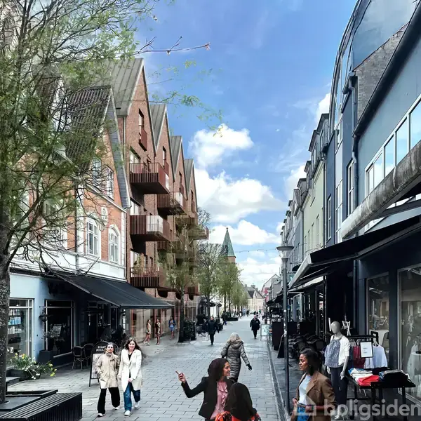 Gågade med folk, der går og handler. Til venstre er der ældre røde murstensbygninger med balkoner, og til højre er der moderne butikker. Træer gror langs vejen under en blå himmel.