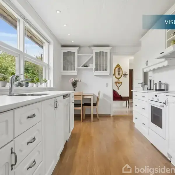 Et hvidt køkken med træbordplade strækker sig langs væggene. Der står gryder på komfuret. Store vinduer giver udsigt til grønne træer udenfor. Tekst: "VISUALISERING".