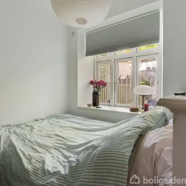 Et køkken med grønne skabe og sort bordplade. Køkkenredskaber og krydderier står på åbne hylder. Rummets åbne dør fører ud til en have, med lys, træ og en stol.