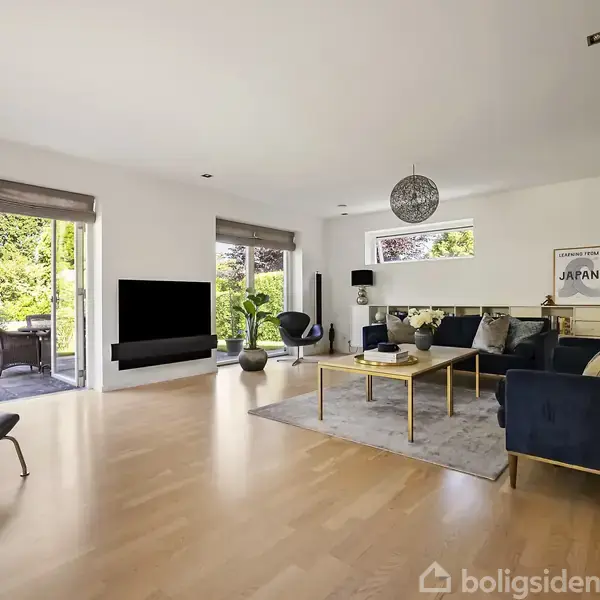Moderne stue med sofaer og sofabord på tæppe, fladskærms-TV på væg; store vinduer viser en terrasse samt have med grønne planter. Plakat med teksten "JAPAN".